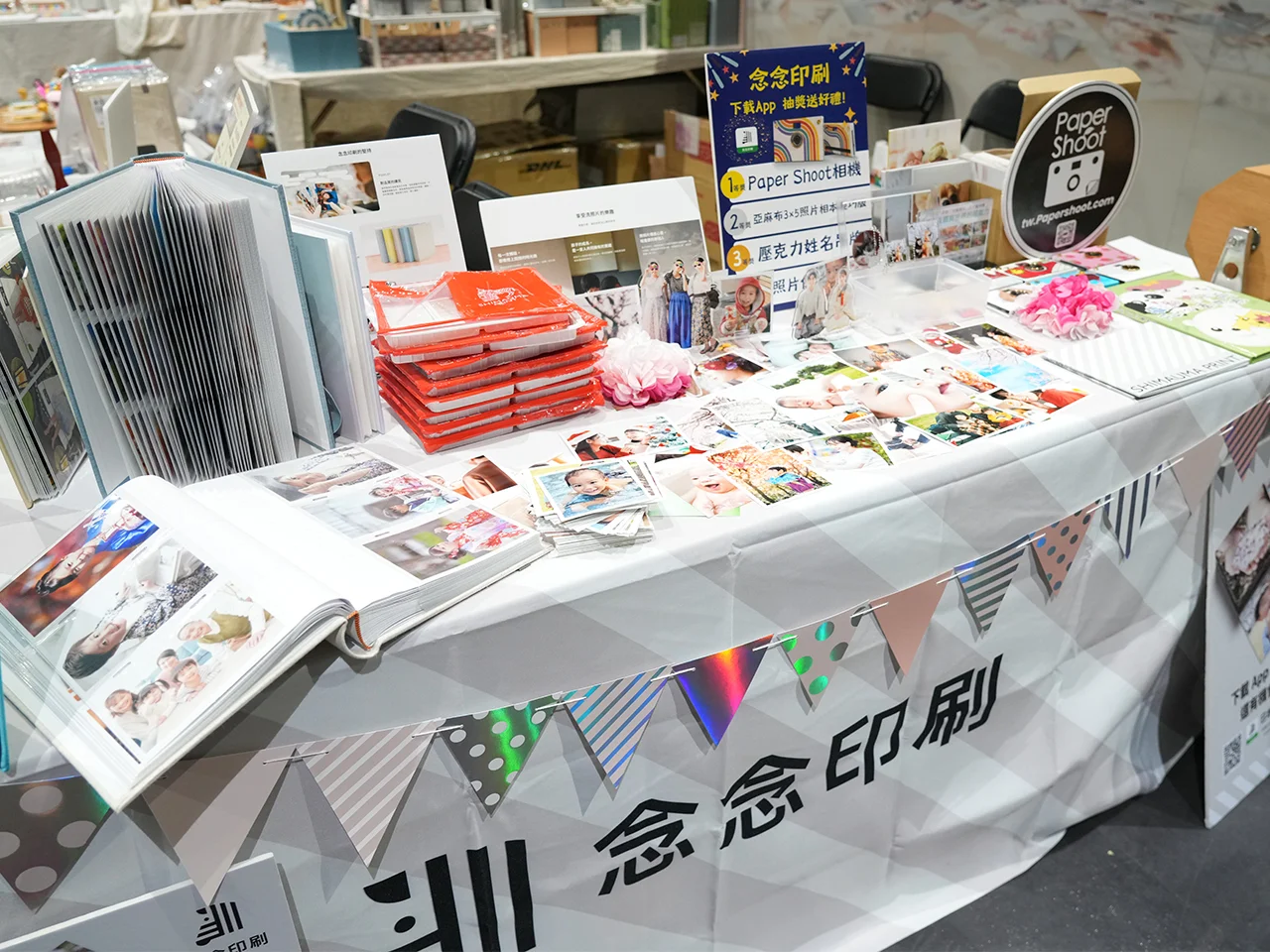 念念印刷展位上的產品陳列近景，包含多款相本、沖印照片，和「線上購物」的客製化壓克力周邊。