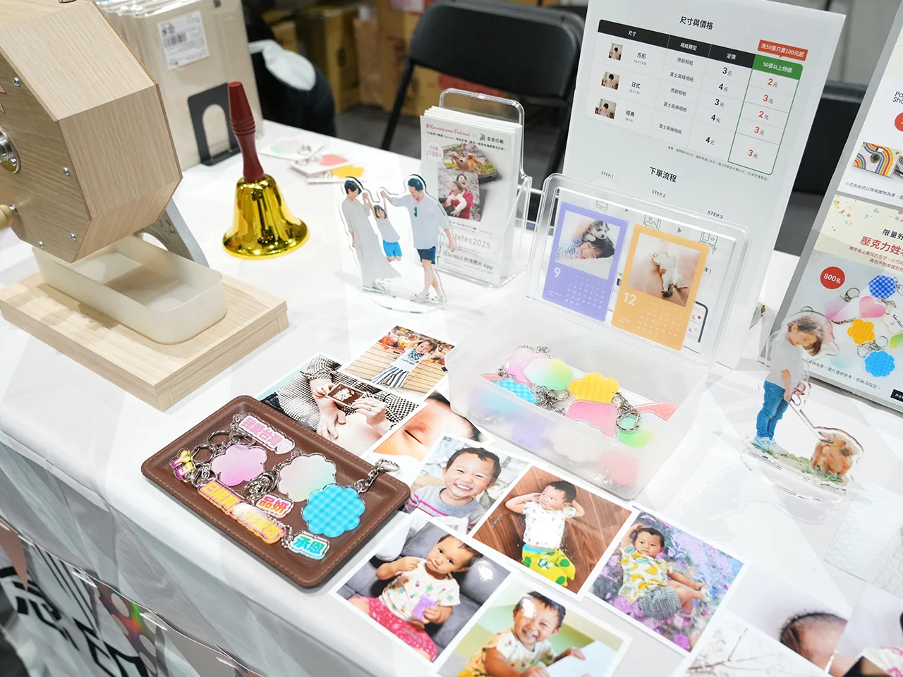 念念印刷展位上展示的客製化商品近景，包括木製抽獎機、壓克力立牌、姓名吊牌、月曆卡和價目表。